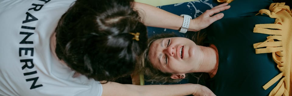 Trainerin begleitet eine liegende Frau während einer intensiven Atemübung
