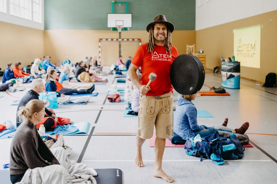 Daniel Fetz steht lächelnd mit Rahmentrommel vor einer Workshop Gruppe